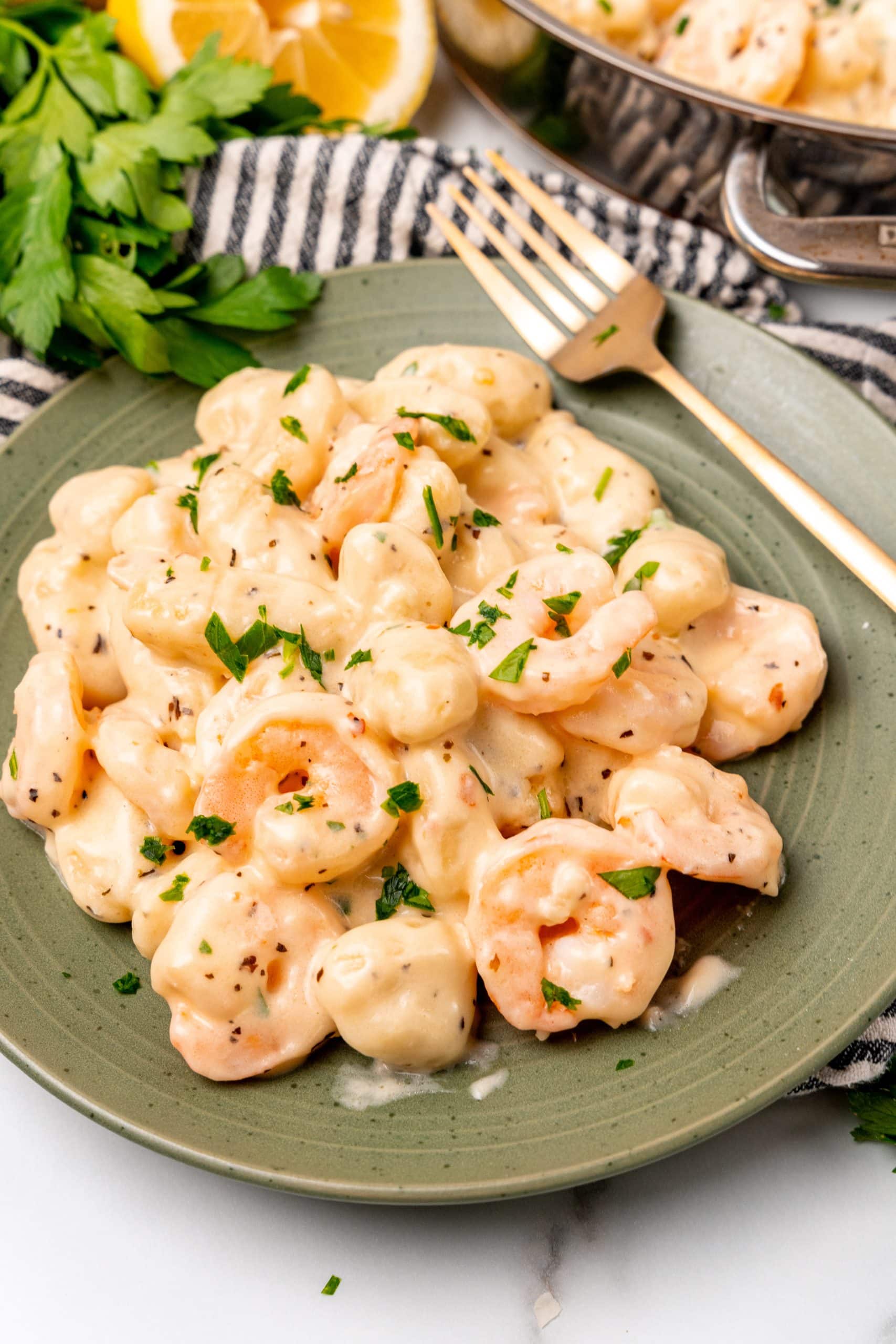 creamy shrimp scampi gnocchi on a green plate with a golden fork resting on the side