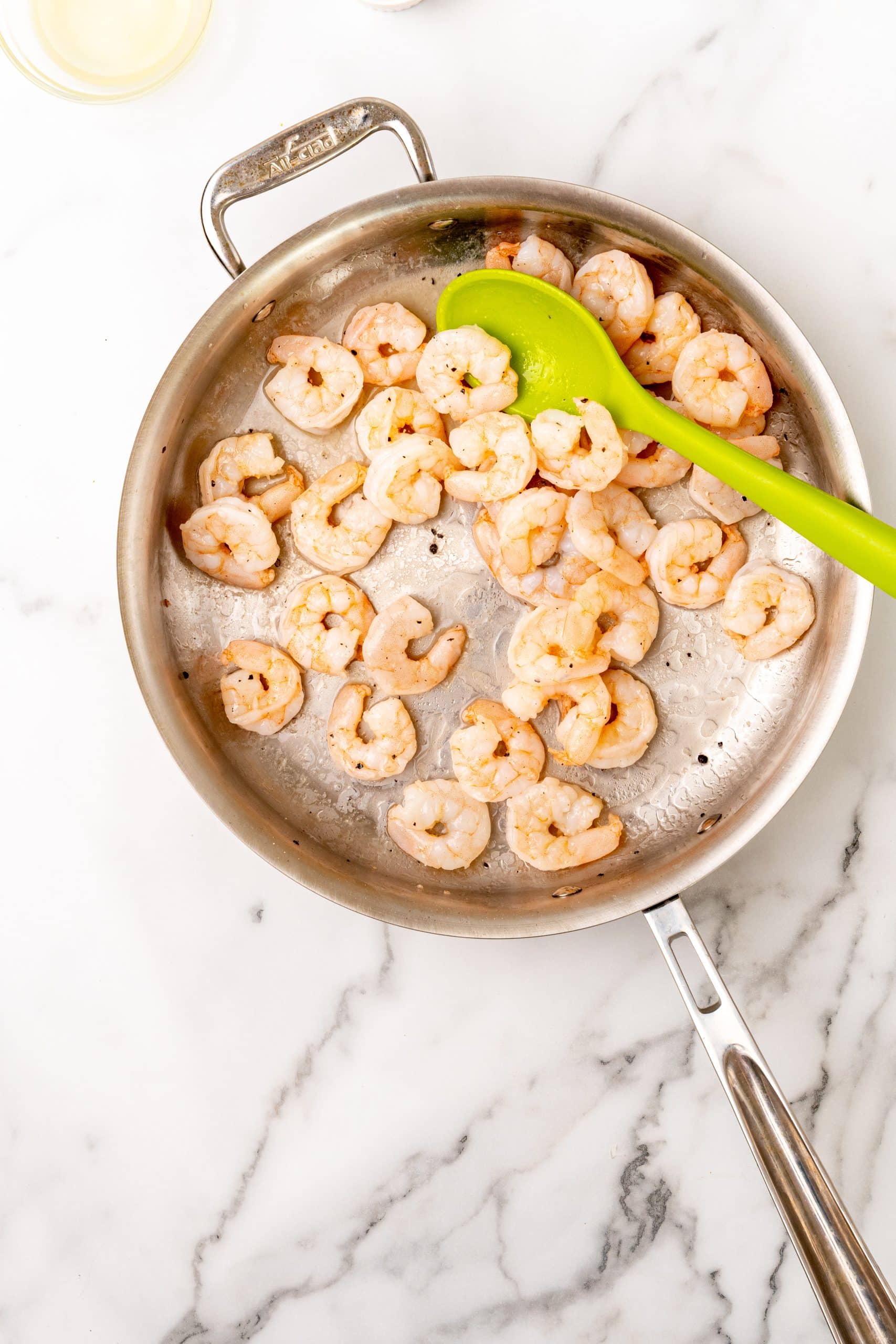 sauteed shrimp in a large silver skillet with a green spoon resting on the side