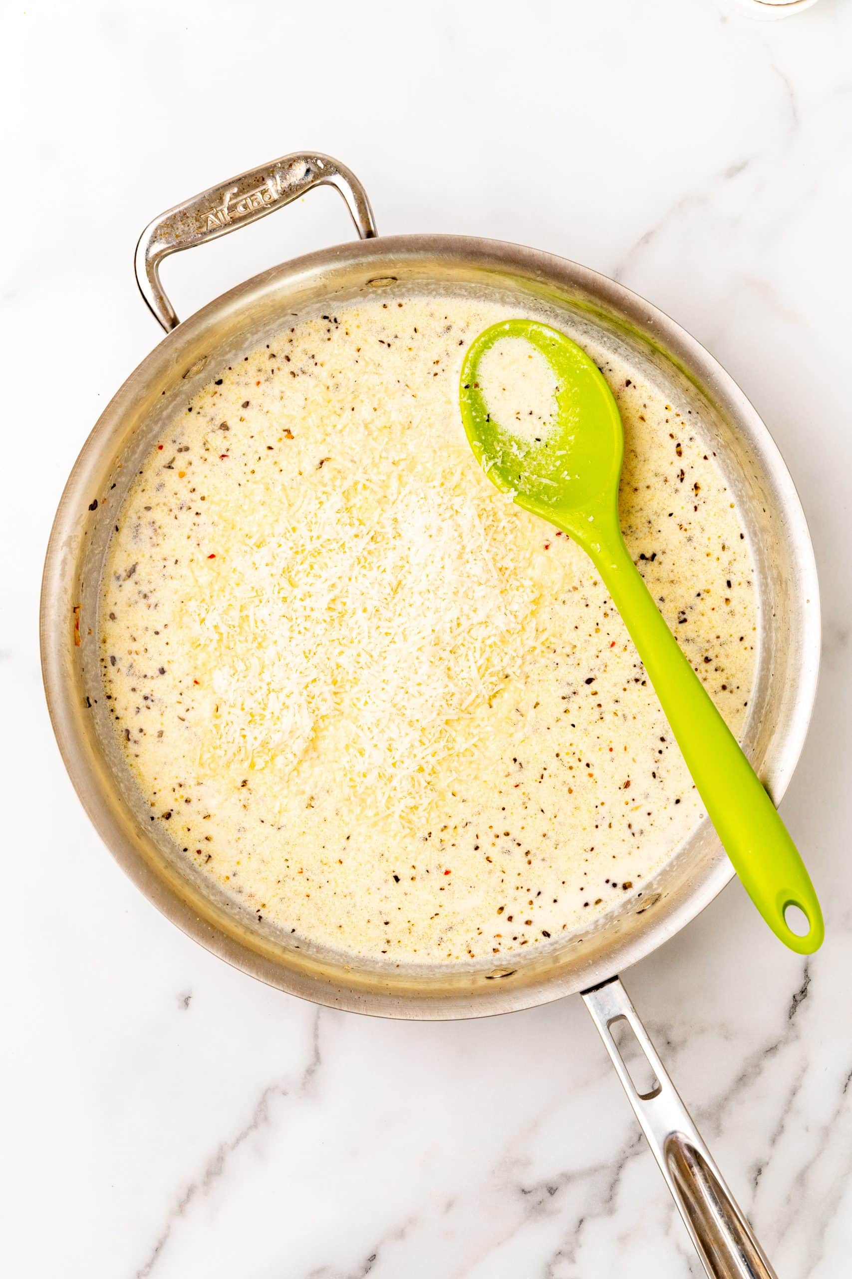 parmesan cheese added to a large silver skillet filled with a creamy garlic butter scampi sauce