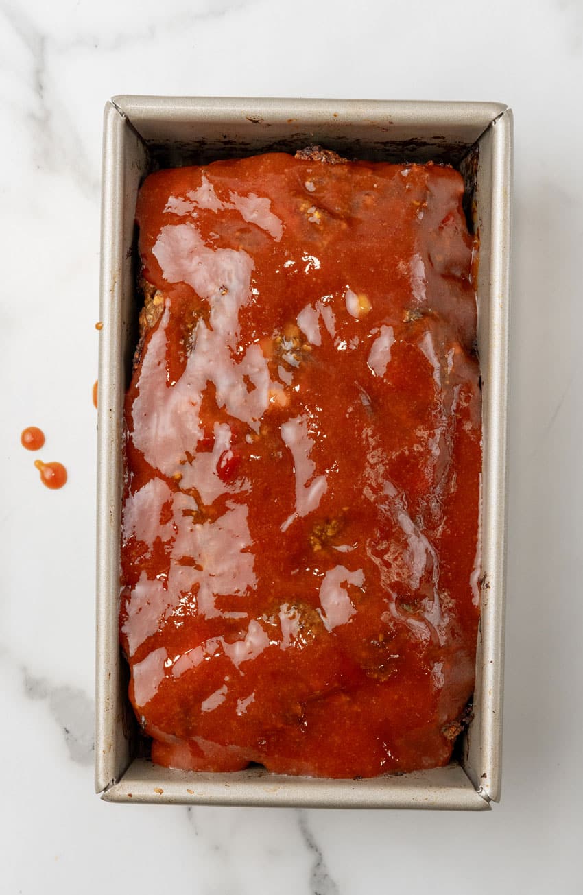 honey barbecue sauce topped mac and cheese stuffed meatloaf in a metal loaf pan