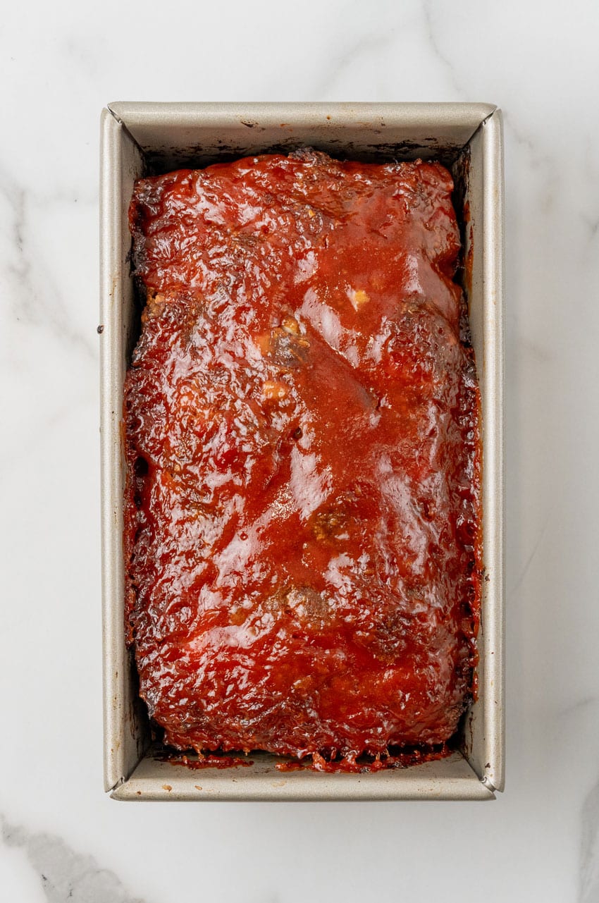 baked honey barbecue sauce topped mac and cheese stuffed meatloaf in a metal loaf pan
