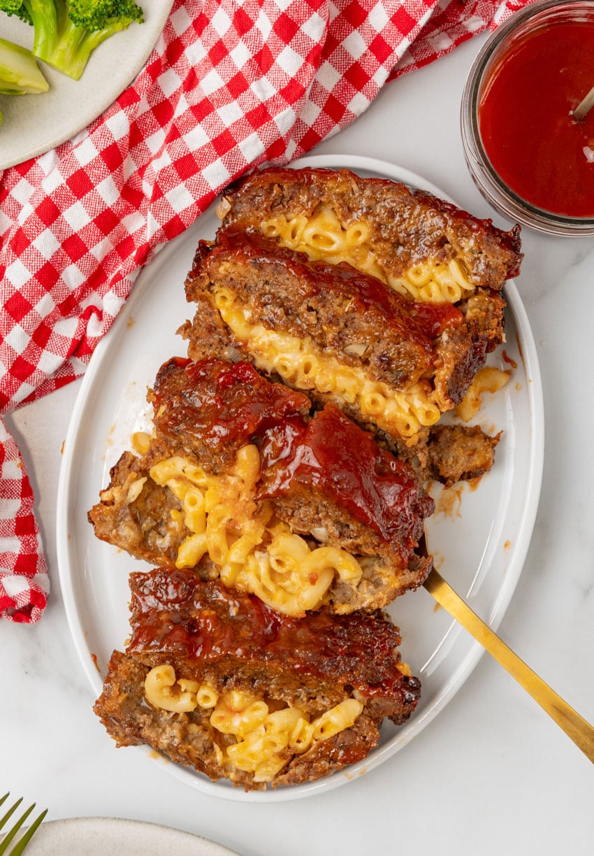 SLICES OF MAC AND CHEESE STUFFED MEATLOAF ARRANGED IN A ROW ON A WHITE SERVING PLATTER