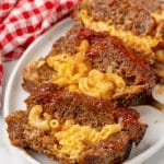 SLICES OF MAC AND CHEESE STUFFED MEATLOAF ARRANGED IN A ROW ON A WHITE SERVING PLATTER