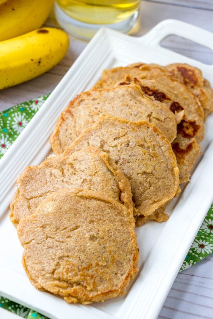 Baby Cereal Pancakes on a rectangular white platter with bananas in the background