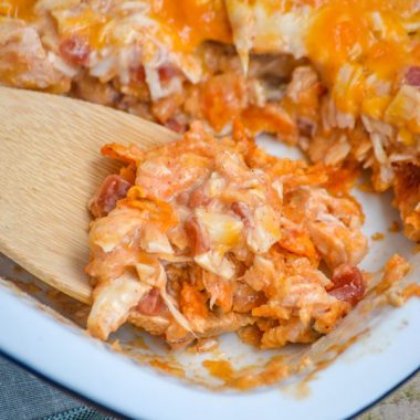 a wooden spoon scooping cheesy doritos chicken casserole from a baking dish