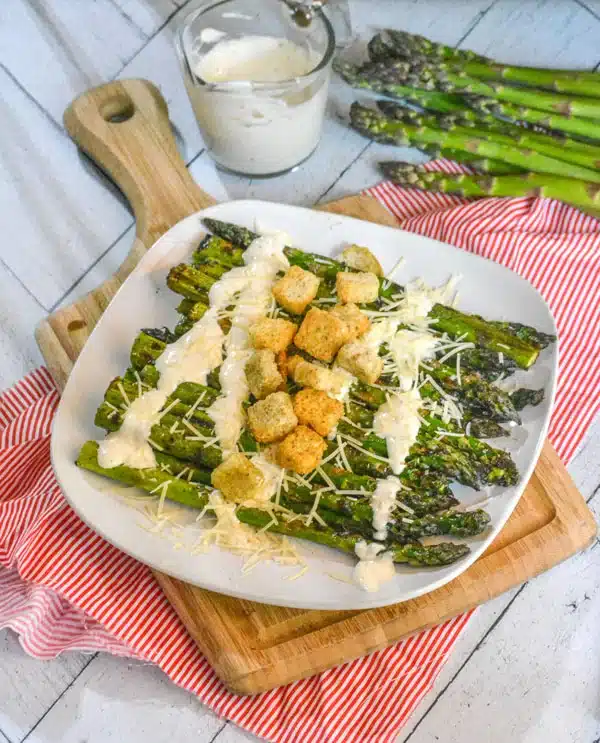 GRILLED CAESAR ASPARAGUS DRIZZED WITH CAESAR DRESSING AND TOPPED WITH CROUTONS ON A WHITE PLATE