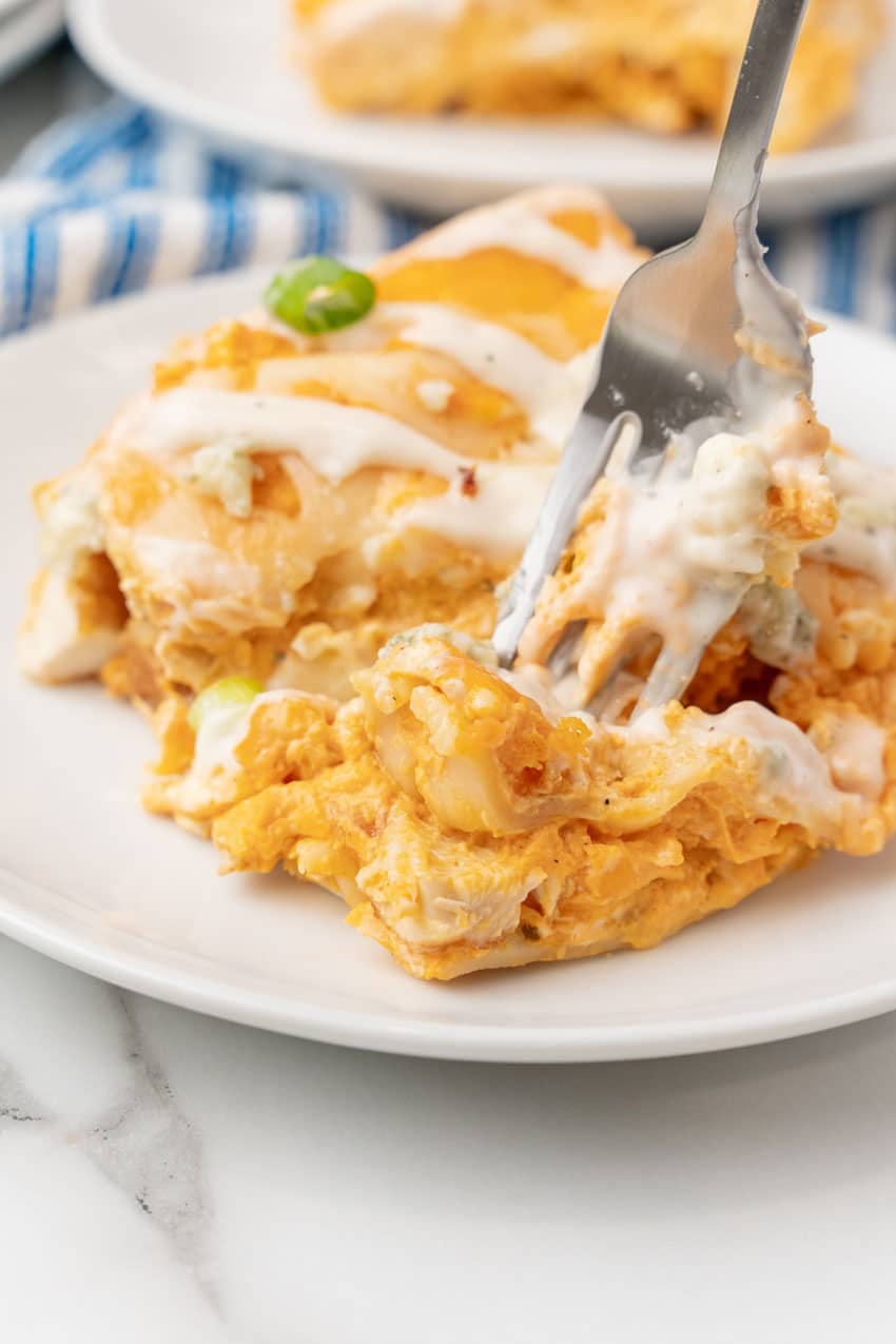 a silver fork digging into a slice of buffalo chicken lasagna on a small white dinner plate