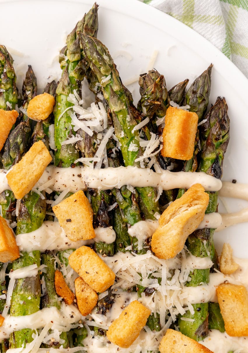 a close up of caesar style grilled asparagus on a white serving plate