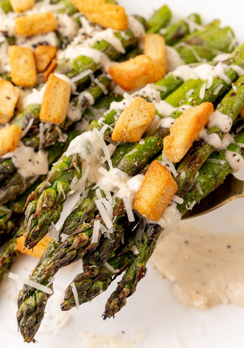 a serving spoon lifting up spears of grilled asparagus drizzled with caesar dressing