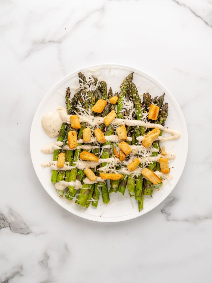 grilled asparagus spears topped with creamy caesar dressing and croutons on a white serving plate