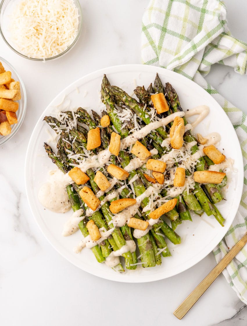grilled asparagus spears topped with creamy caesar dressing and croutons on a white serving plate