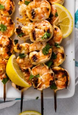 grilled nam prik shrimp skewers stacked on a white square plate with fresh lemon wedges