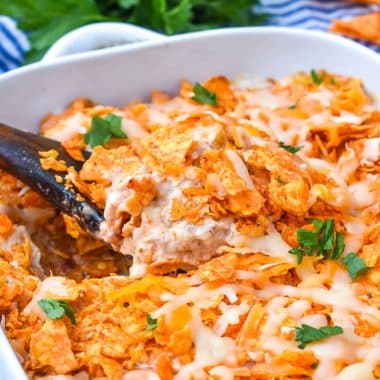 a wooden spoon scooping chicken doritos casserole out a white dish