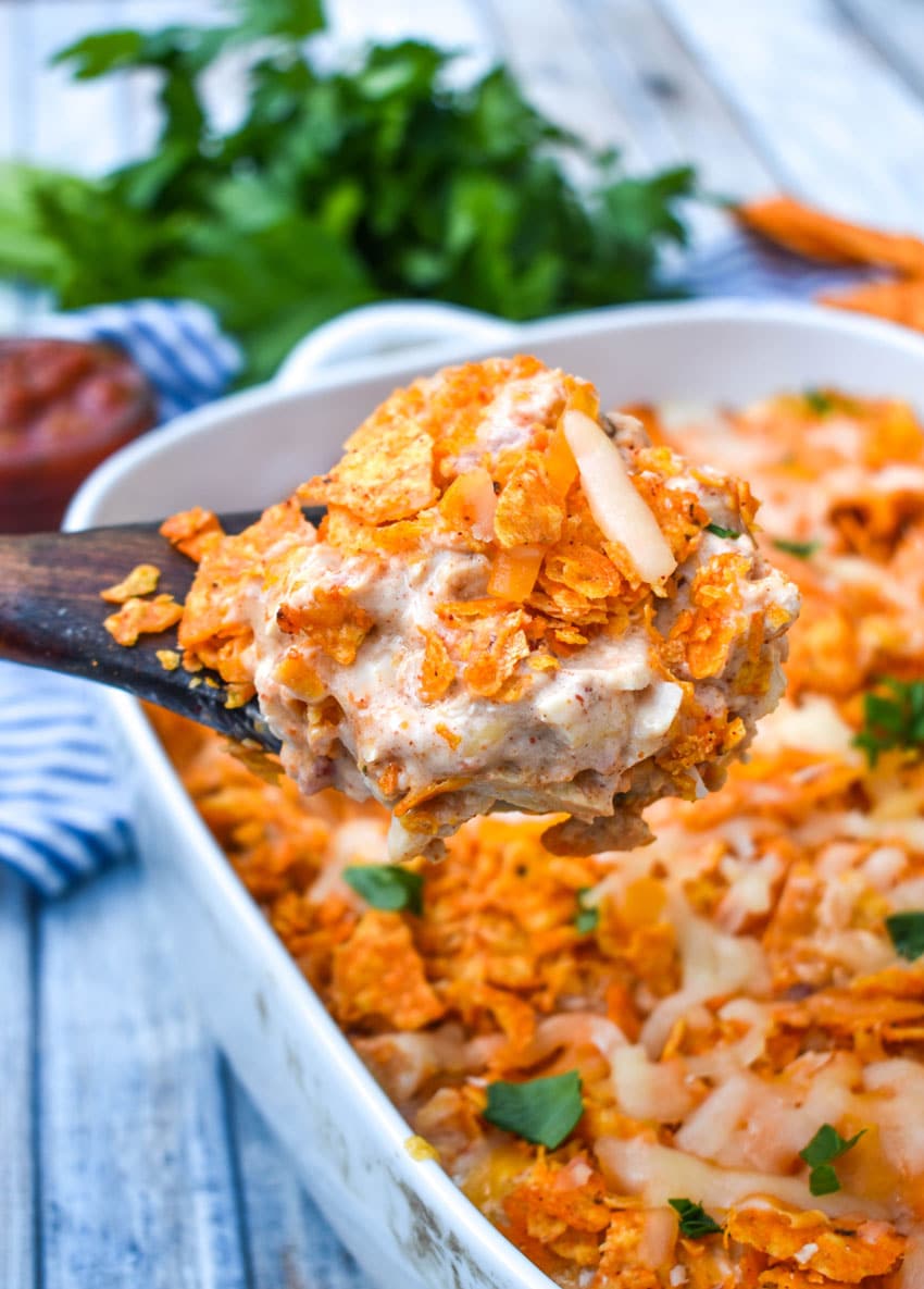 a wooden spoon scooping chicken doritos casserole out a white dish