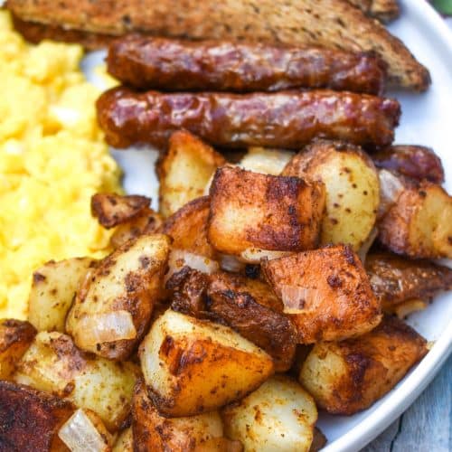 DINER STYLE HOME FRIED BREAKFAST POTATOES ON A WHITE PLATE ALONG WITH SCRAMBLED EGGS, SAUSAGE LINKS, AND TOAST