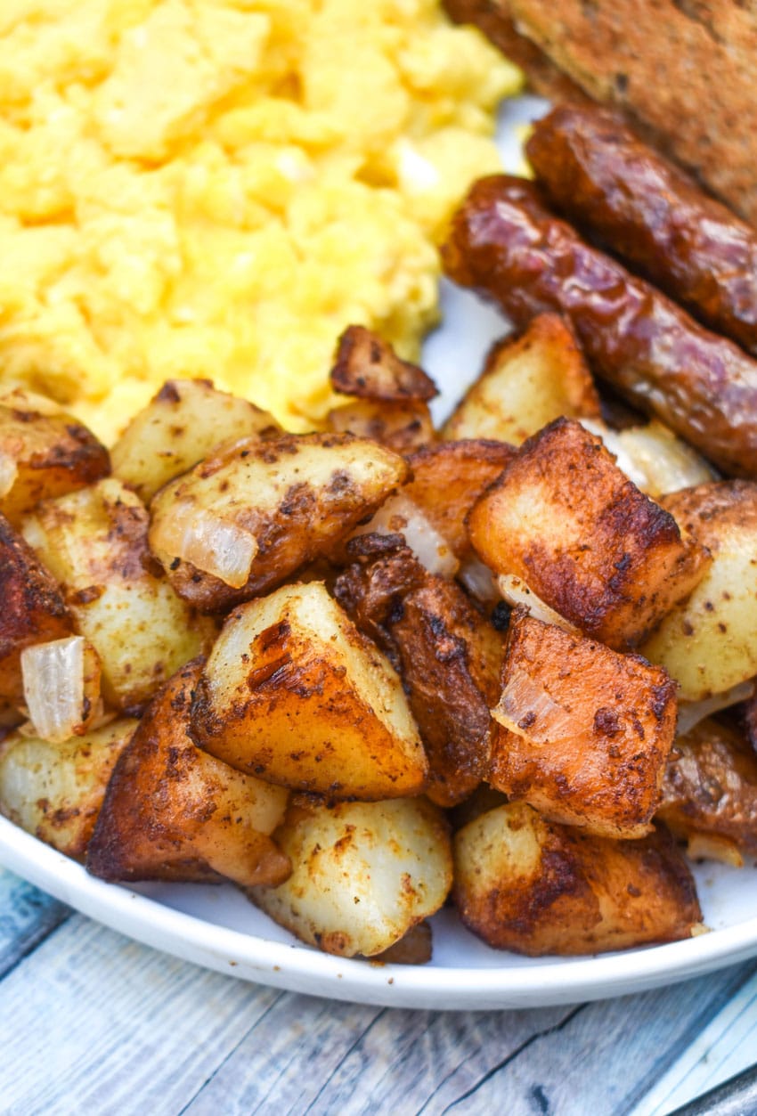 DINER STYLE HOME FRIED BREAKFAST POTATOES ON A WHITE PLATE ALONG WITH SCRAMBLED EGGS, SAUSAGE LINKS, AND TOAST