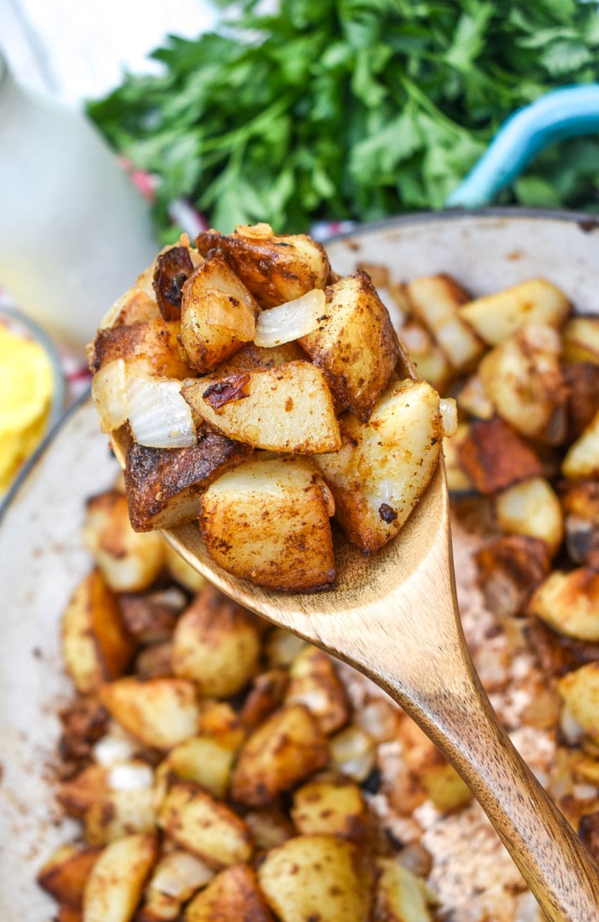 a wooden spoon holding up a scoop of home fried breakfast potatoes recipe