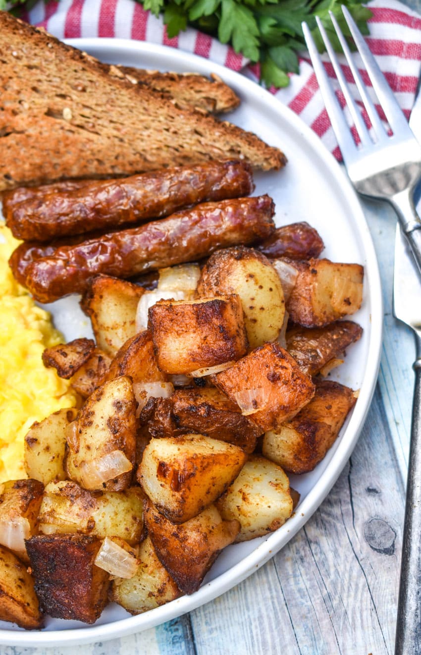 DINER STYLE HOME FRIED BREAKFAST POTATOES ON A WHITE PLATE ALONG WITH SCRAMBLED EGGS, SAUSAGE LINKS, AND TOAST