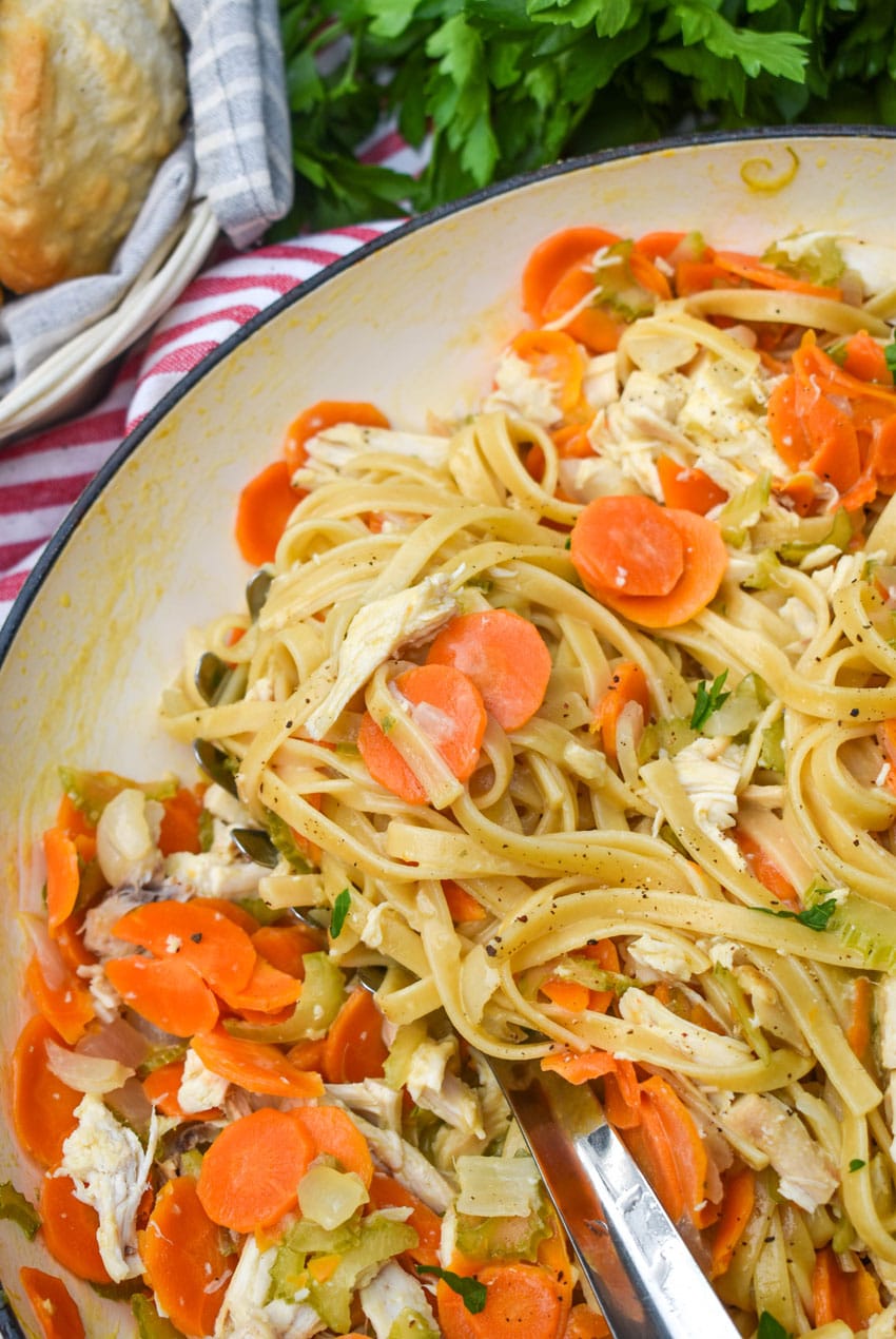 a silver spoon scooping a creamy one pot chicken pasta with vegetables out of a large white cast iron skillet