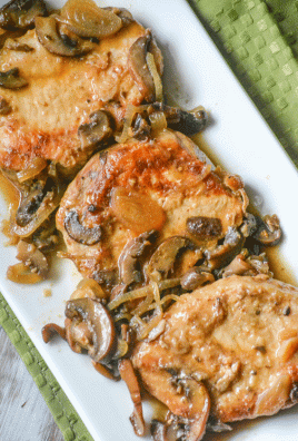 marsala pork chops topped with shallots and mushrooms lined up on a white serving platter