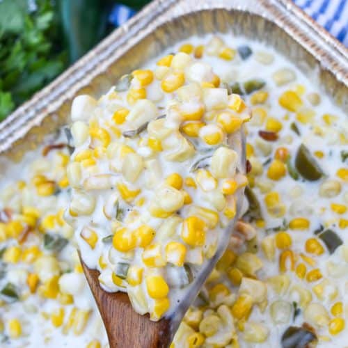 a wooden spoon holding up a scoop of smoked jalapeno cheddar creamed corn