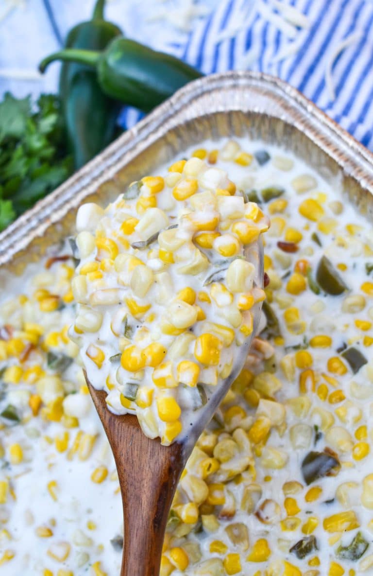 a wooden spoon holding up a scoop of smoked jalapeno cheddar creamed corn