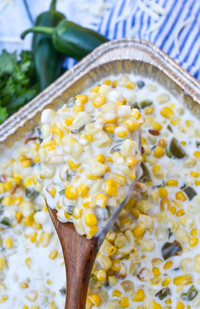 a wooden spoon holding up a scoop of smoked jalapeno cheddar creamed corn