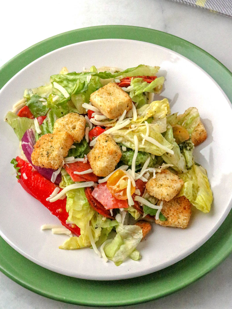 pepperoni pizza salad served on a white plate resting on a larger green plate