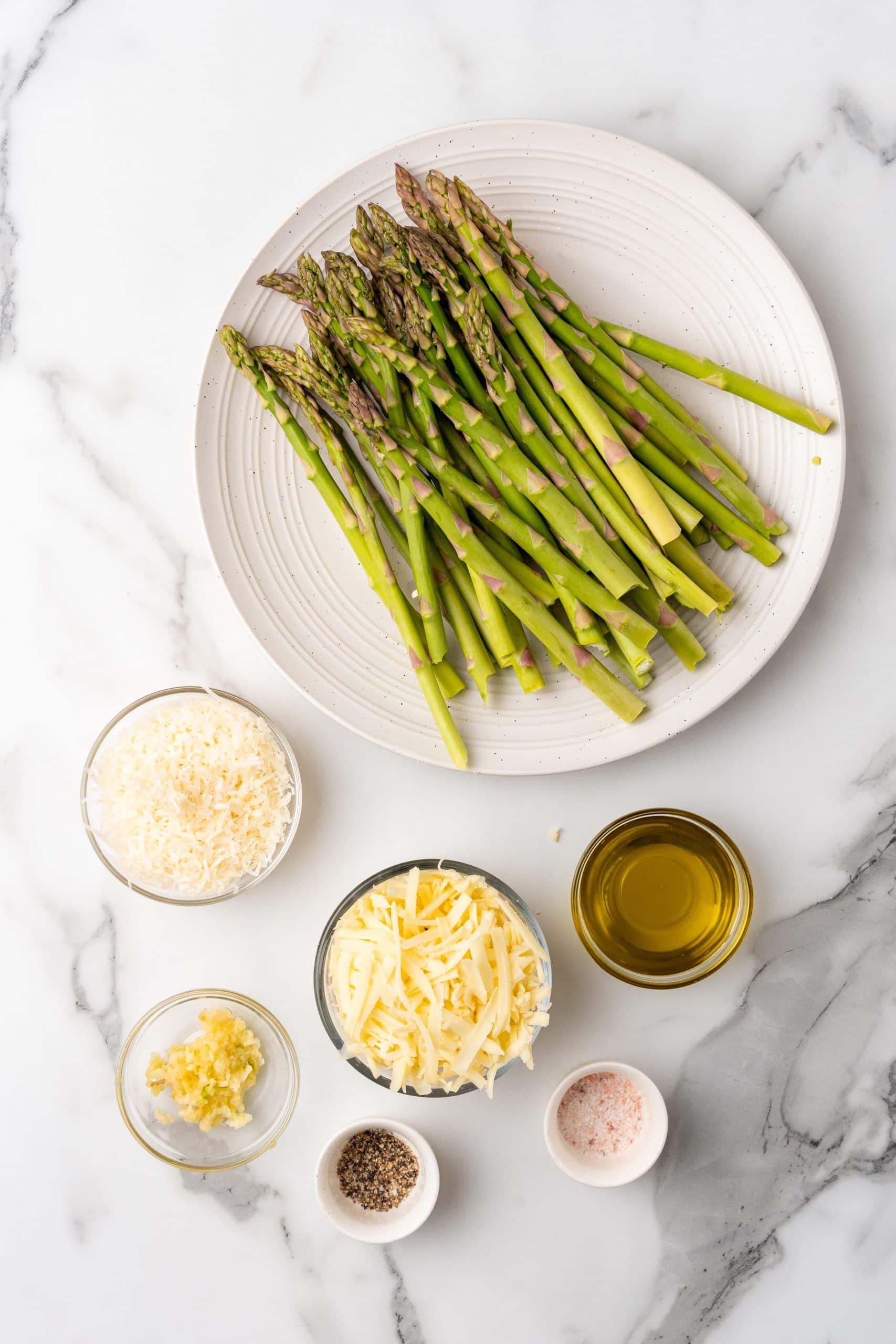 an overhead image showing the measured ingredients to make a batch of cheesy garlic roasted asparagus on a sheet pan