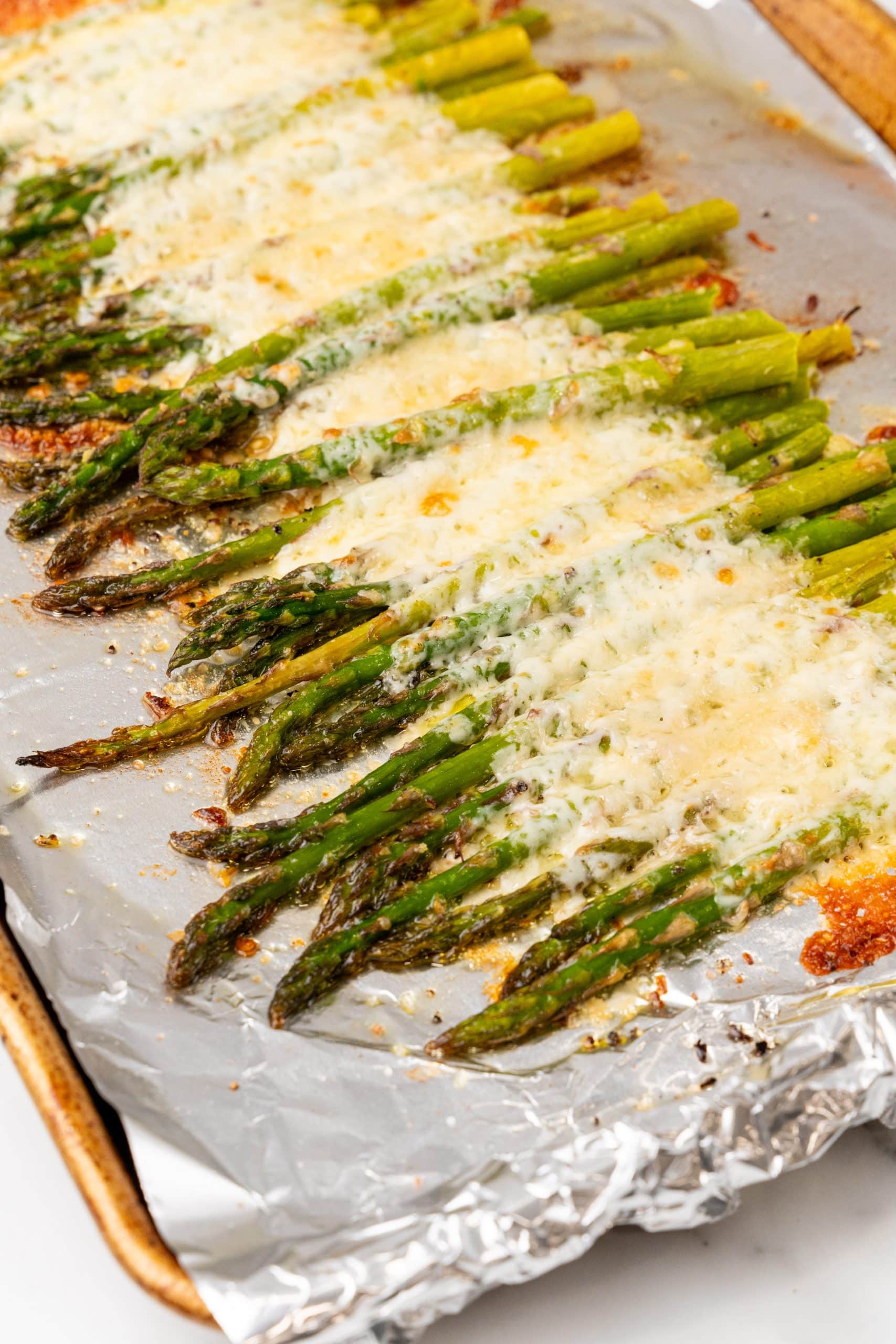 cheesy garlic roasted asparagus arranged in a row on a foiled lined sheet pan