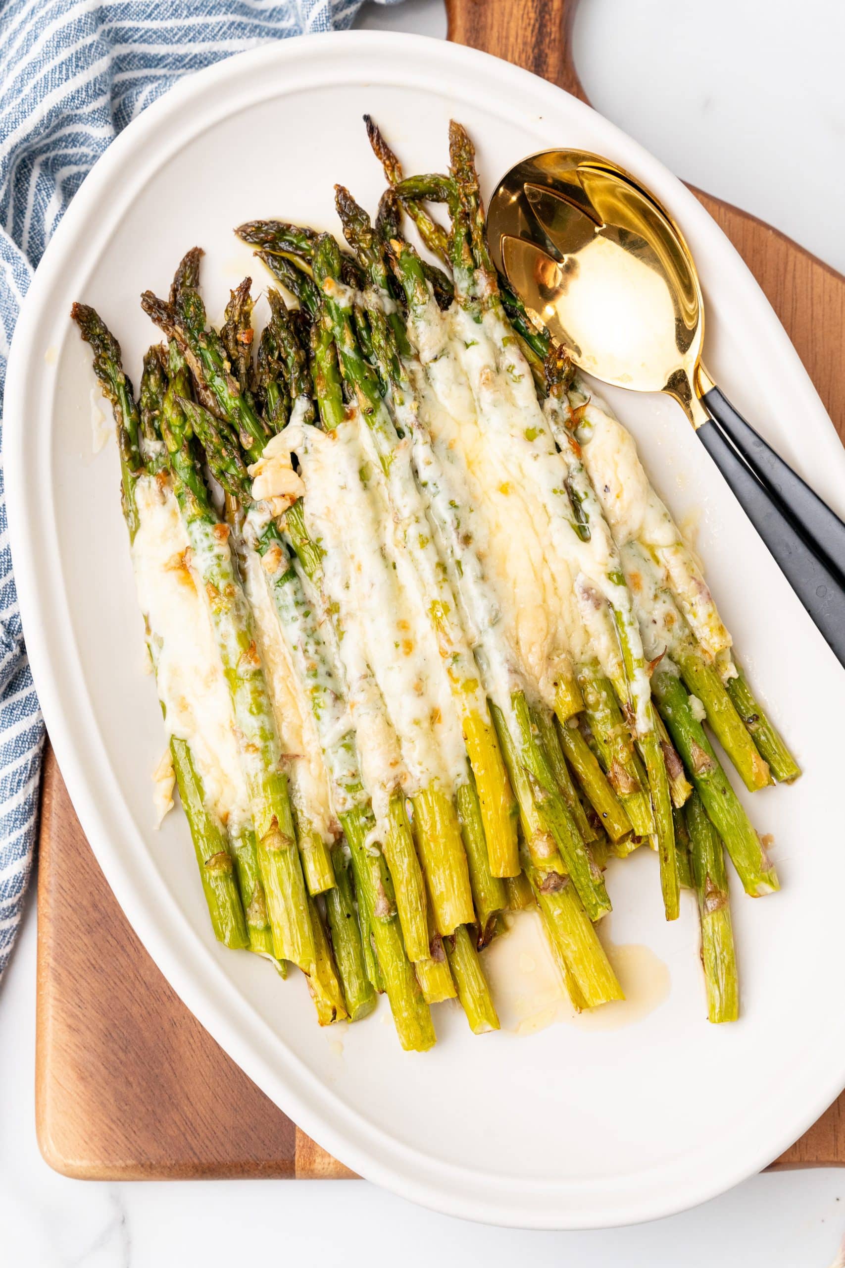 cheesy garlic roasted asparagus on a white serving platter resting on a wooden cutting board