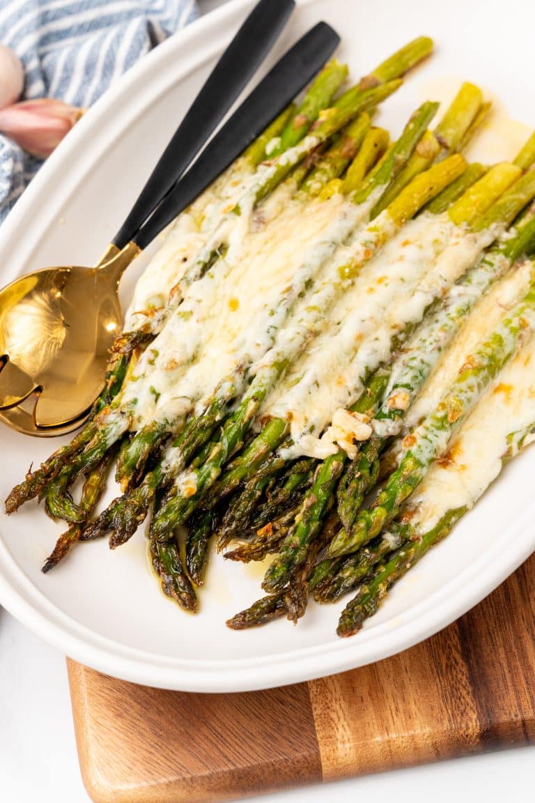 cheesy garlic roasted asparagus on a white serving platter resting on a wooden cutting board