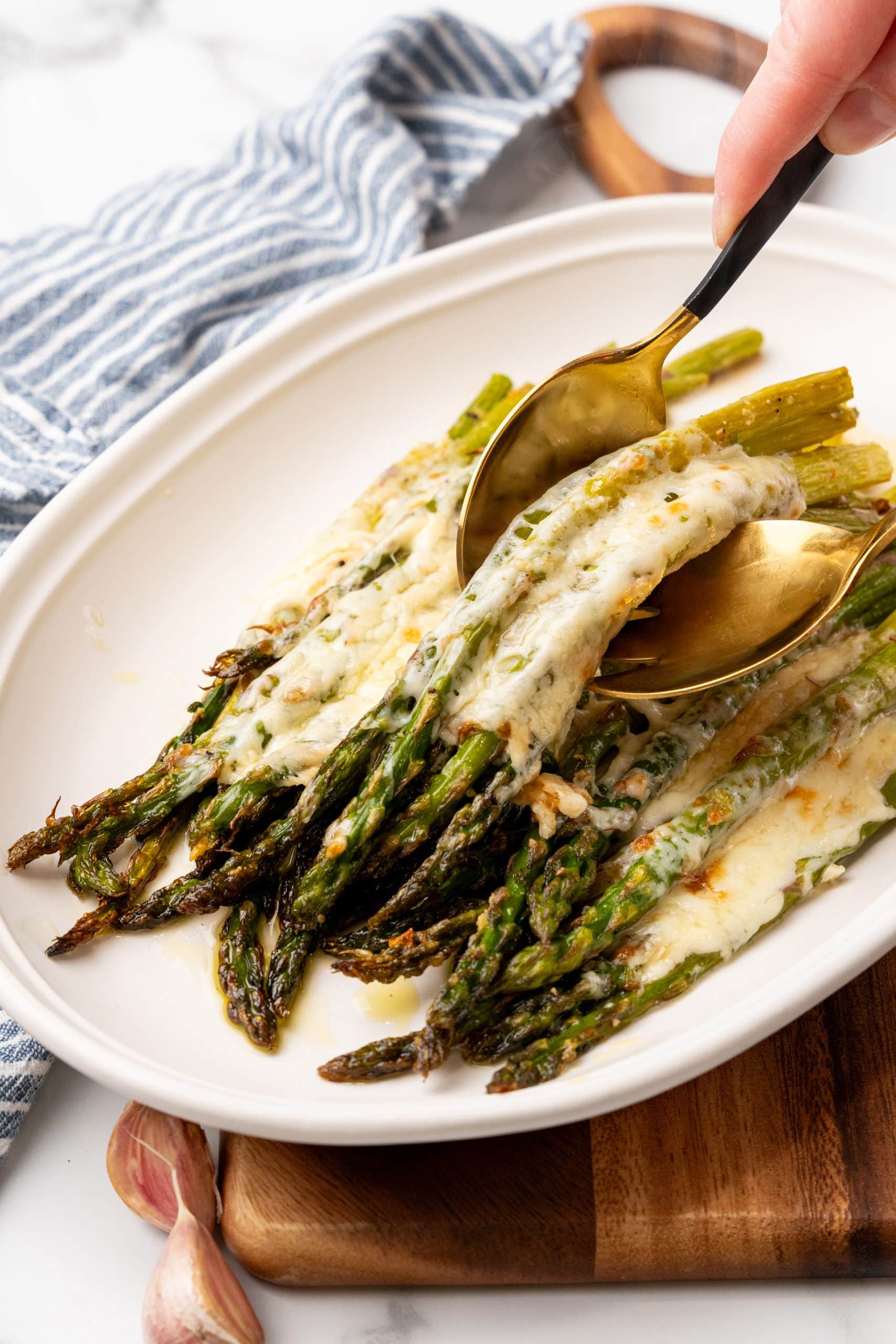 two golden salad forks lifting cheesy garlic roasted asparagus off a white serving platter