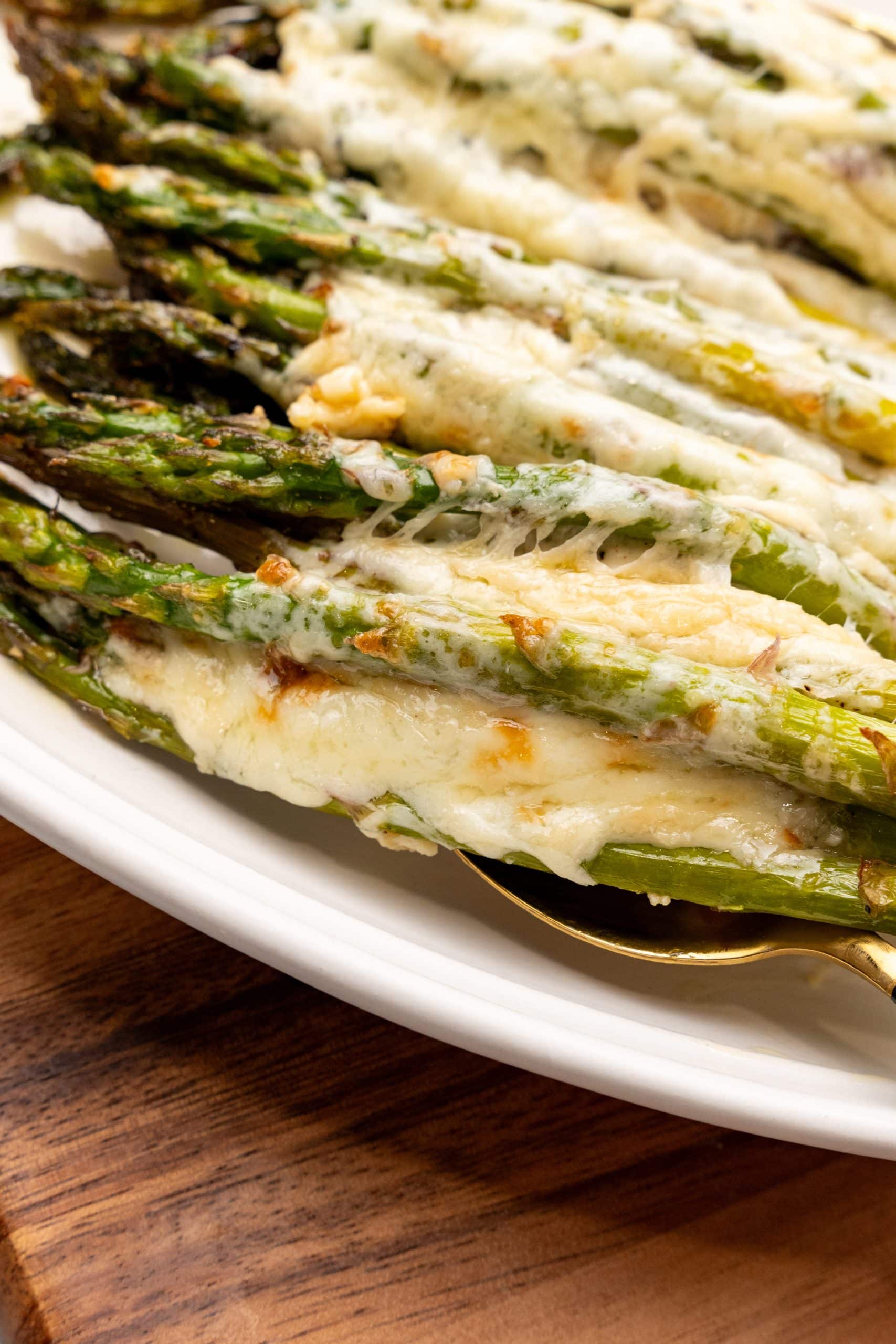 a spoon lifting cheesy garlic roasted asparagus off a white serving platter