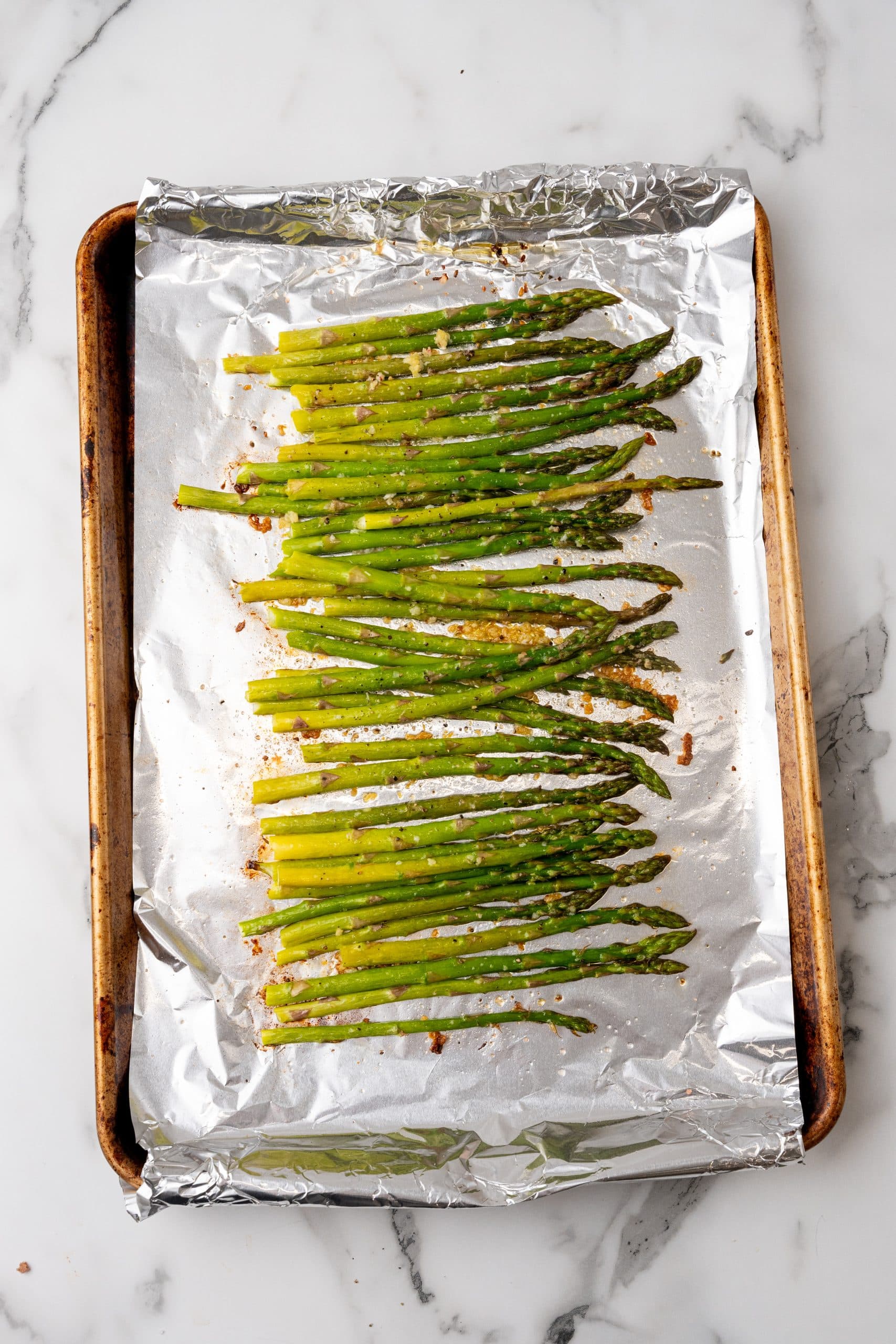 garlic roasted asparagus arranged in a single row on a foil lined baking sheet