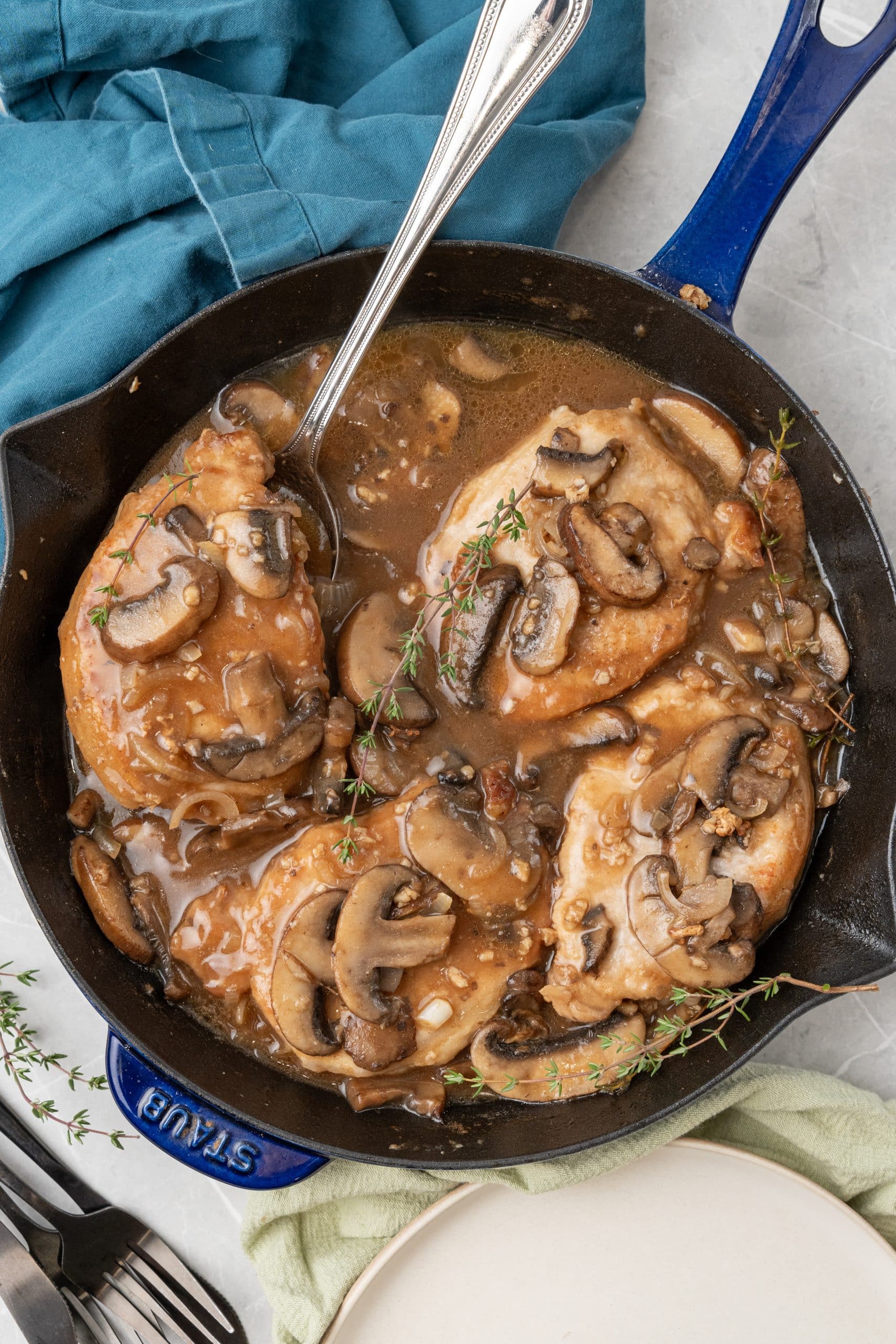 a silver serving spoon resting in a cast iron skillet filled with pork chop marsala with mushrooms and onion
