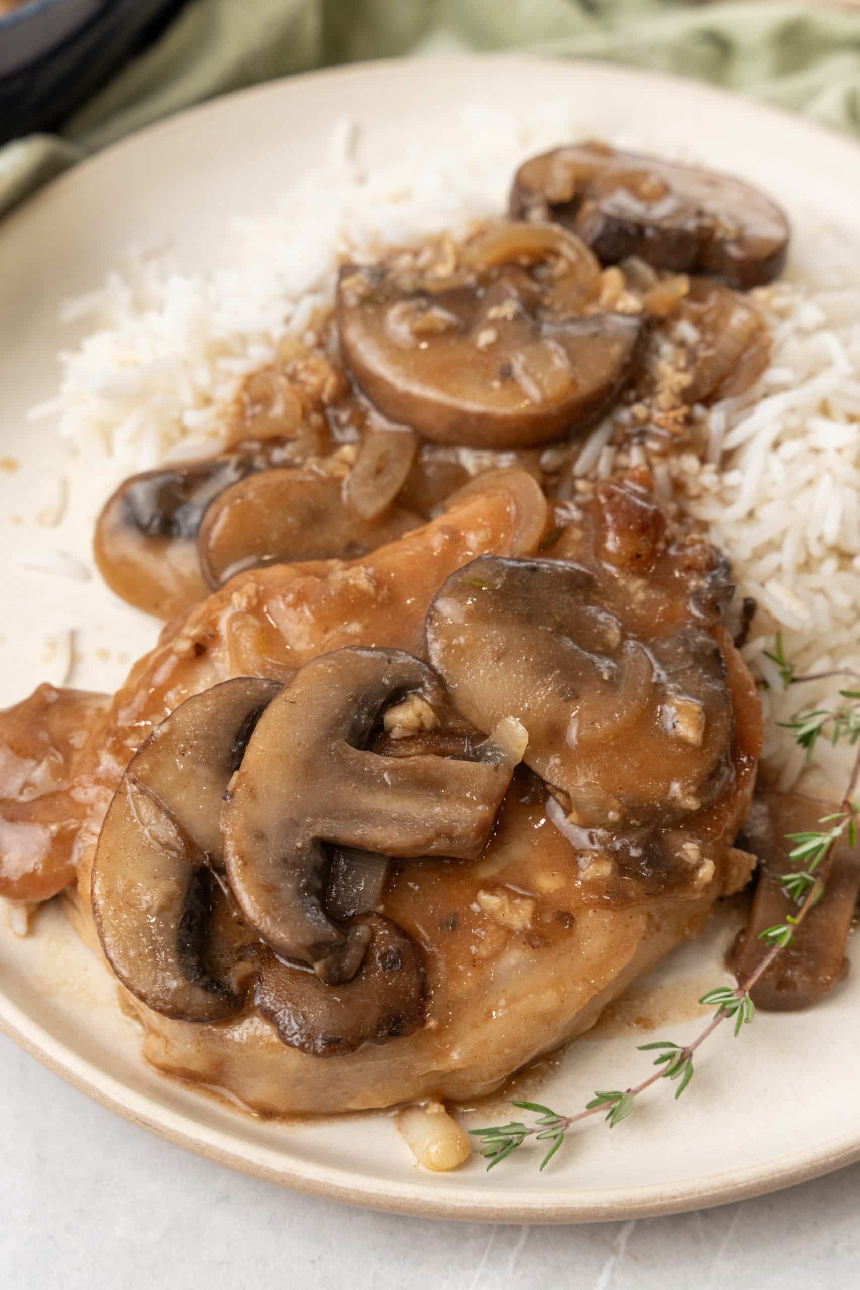 a piece of marsala pork covered in mushroom and onion gravy on a bed of white rice on a white plate