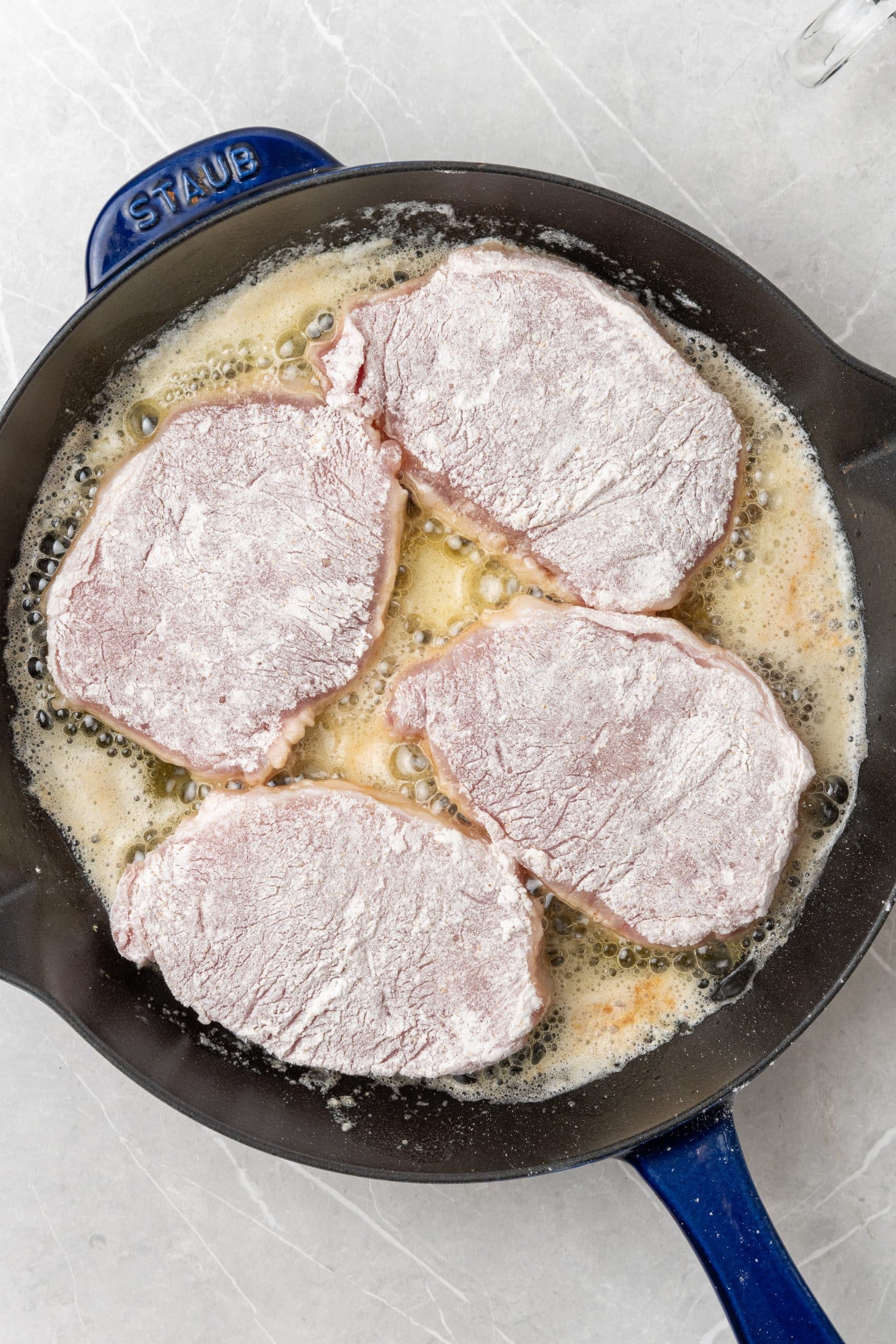 four flour dredged pork chops in a cast iron skillet with melted butter