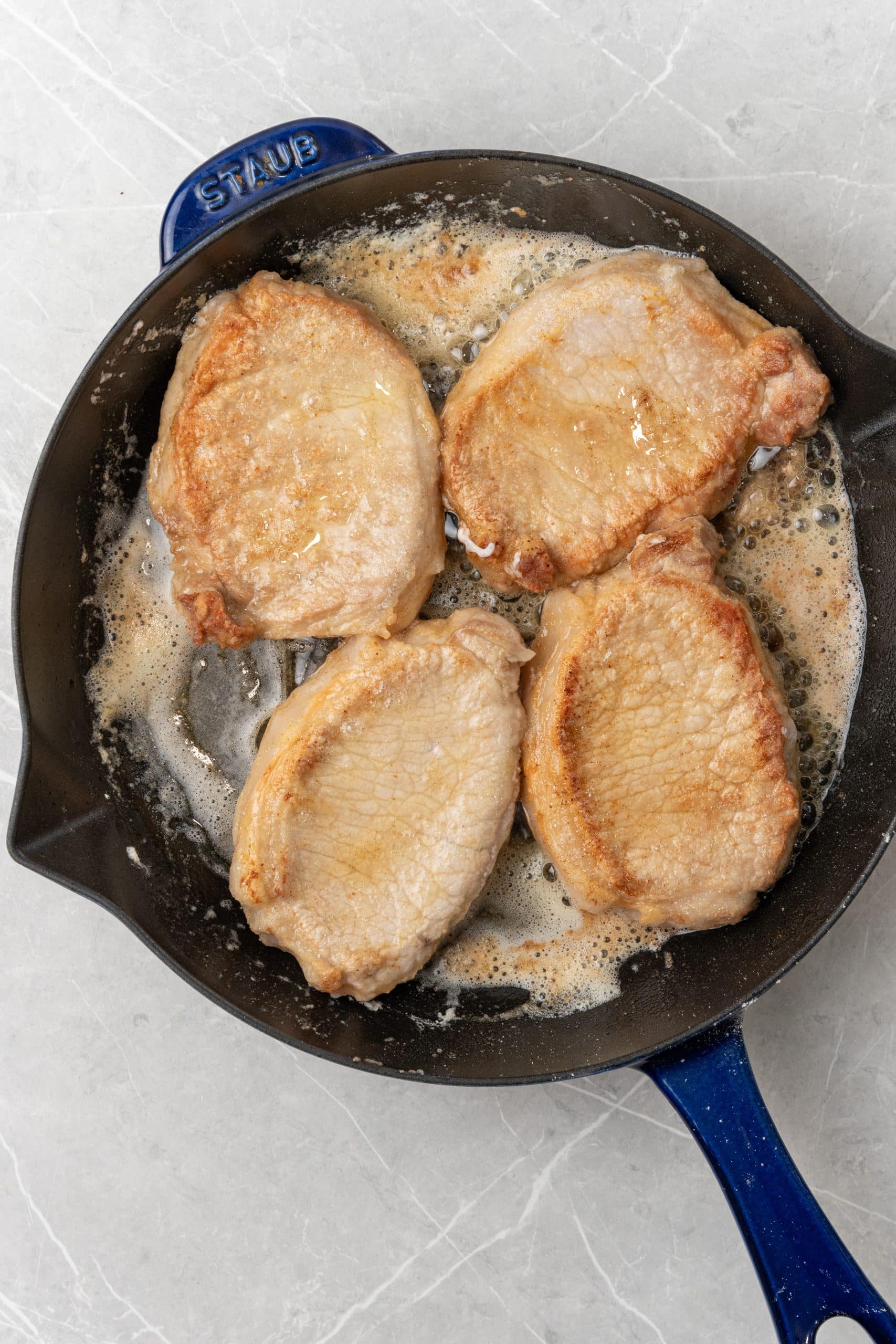 seared pork chops cooking in hot butter in a cast iron skillet