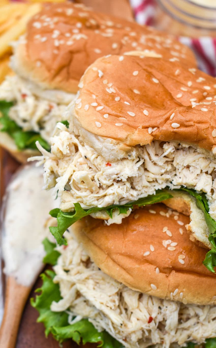 easy crock pot chicken caesar sandwiches stacked on a wooden cutting board
