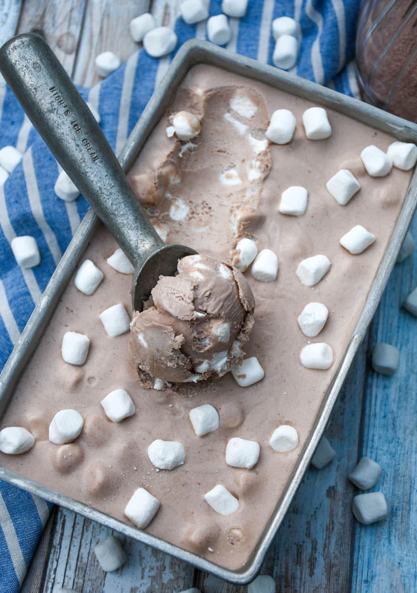a metal ice cream scoop scooping frozen hot chocolate ice cream out of a metal loaf pan