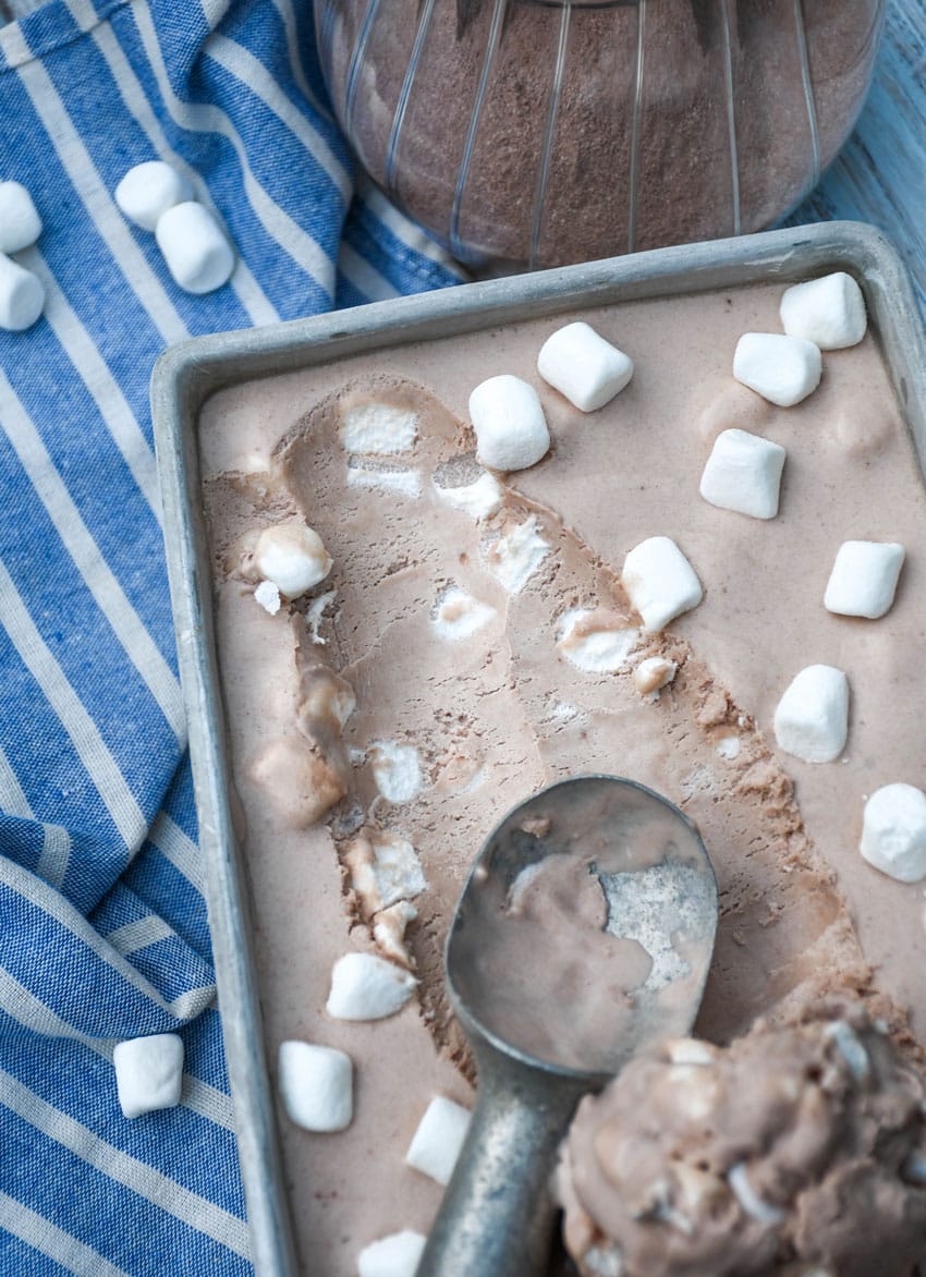 a metal ice cream scoop scooping frozen hot chocolate ice cream out of a metal loaf pan