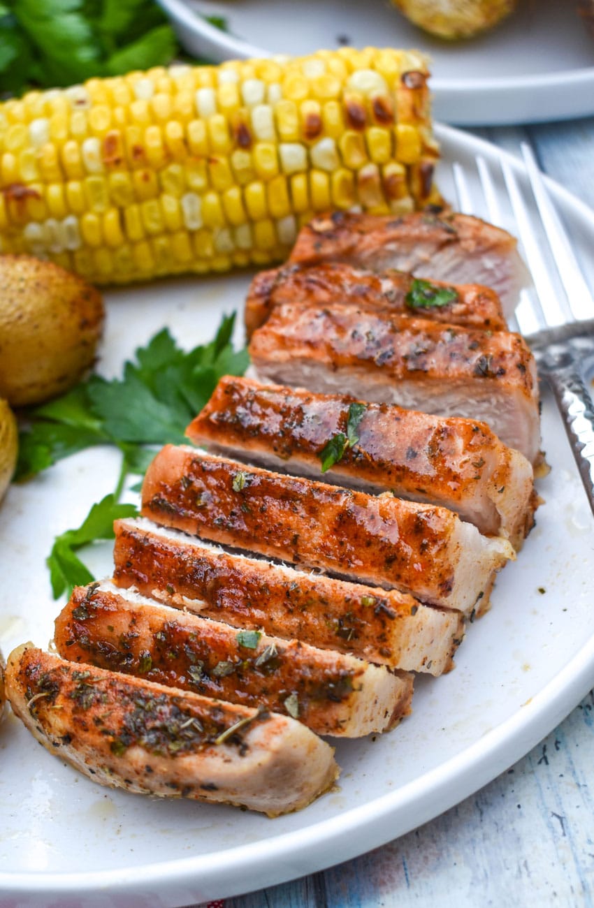 a sliced ranch pork chop topped on a white plate with potatoes and corn on the cob on the side