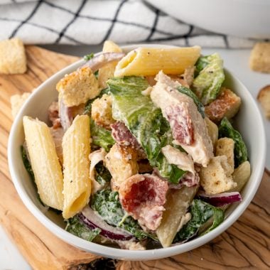 chicken caesar pasta salad in a small white bowl on a wooden cutting board