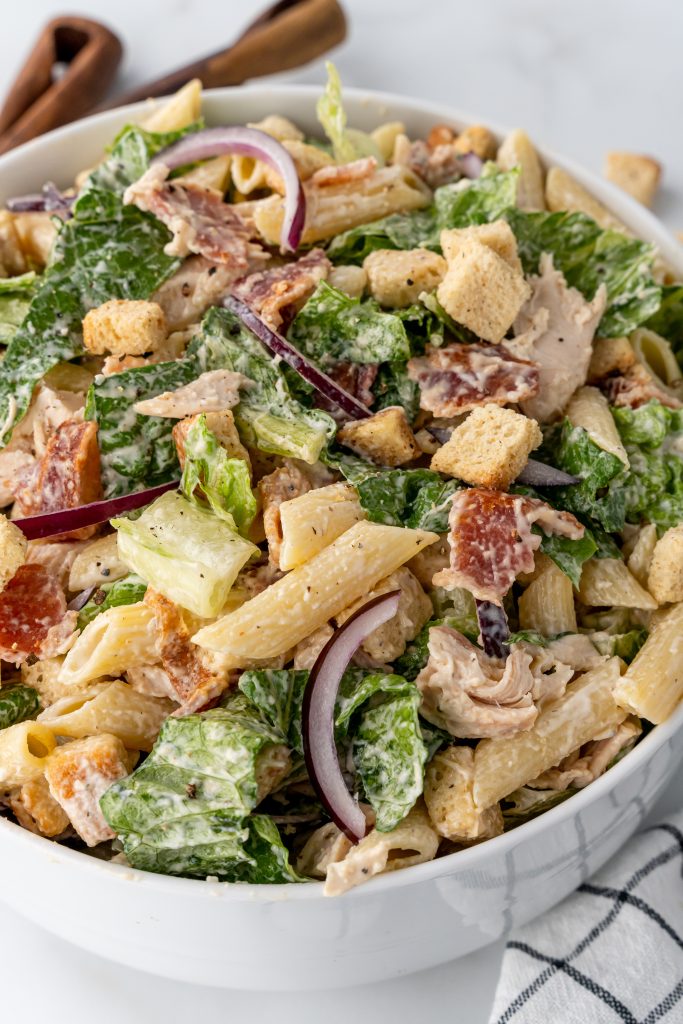 chicken caesar pasta salad in a large white mixing bowl