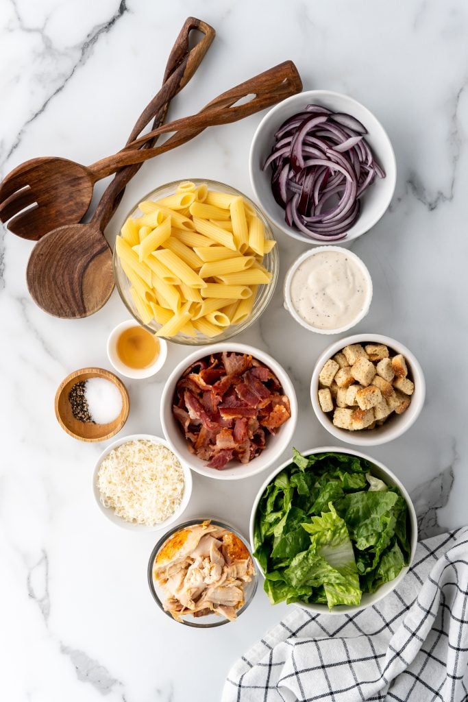 overhead image showing the measured ingredients needed for a batch of chicken caesar pasta salad