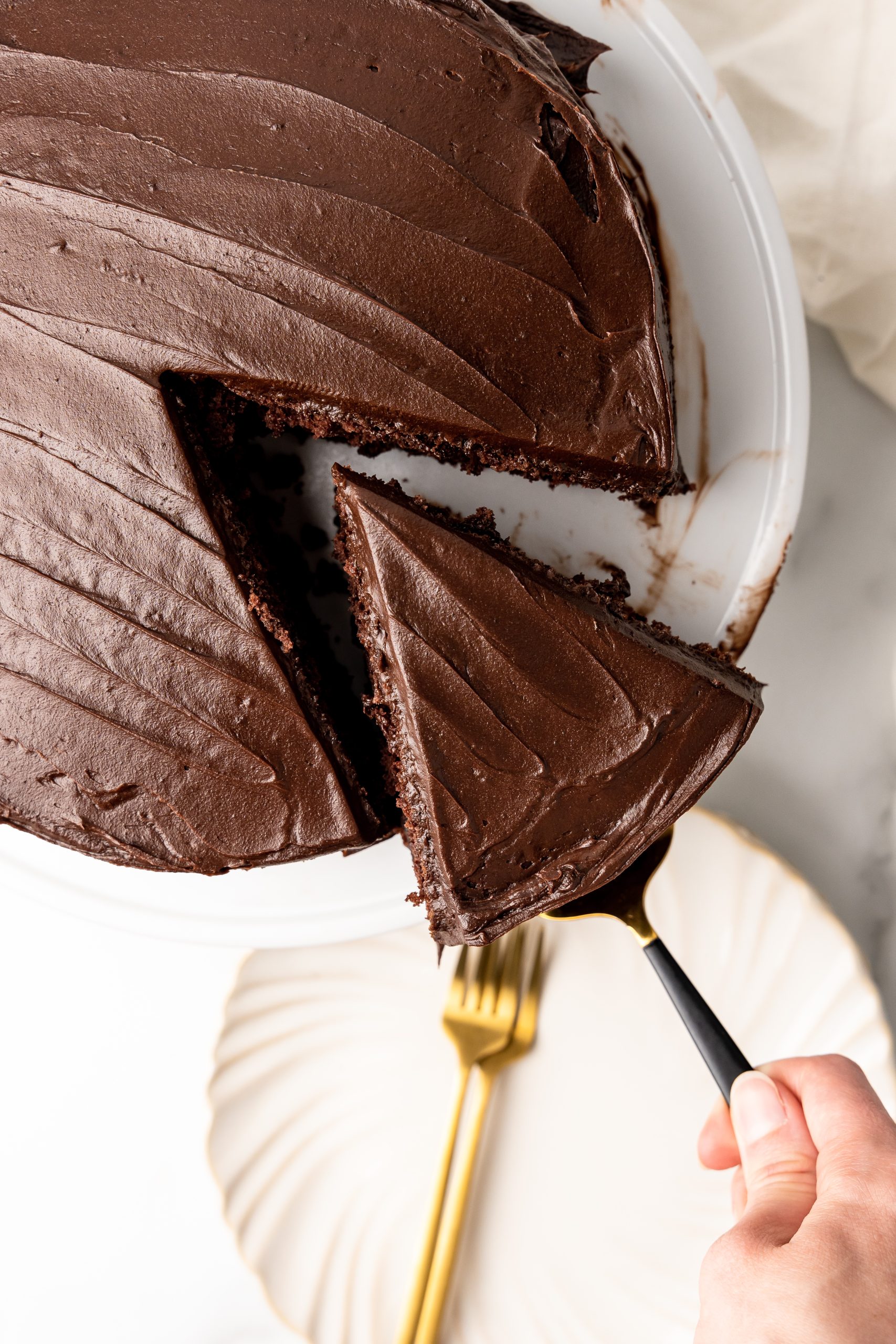 a cake server removing a slice of frosted chocolate church cake from a white pedestal
