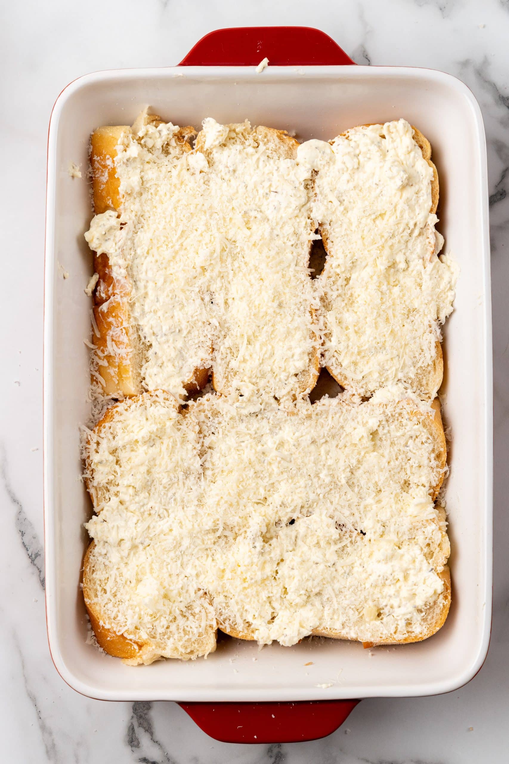 Parmesan cheese spread over cream cheese covered slices of bread in a large baking dish