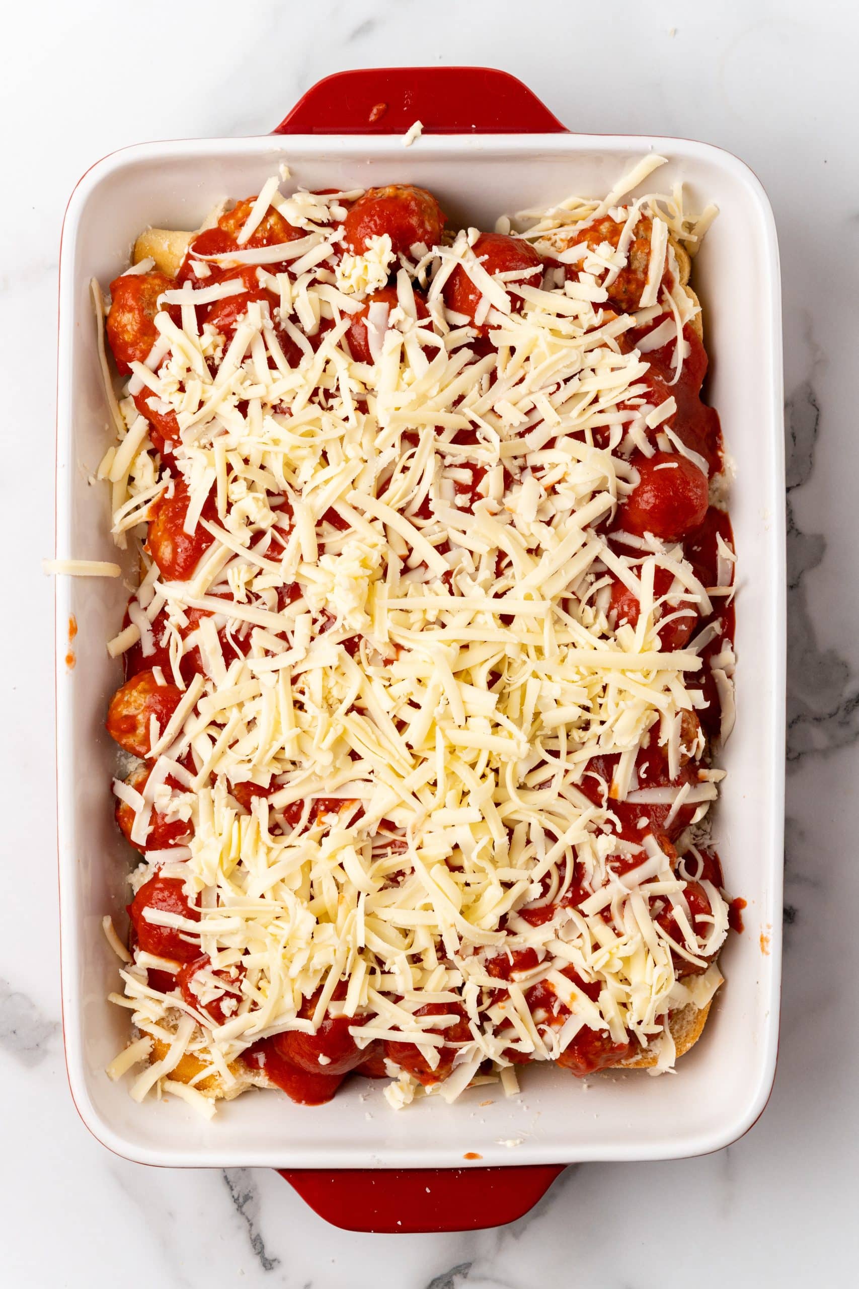 shredded cheese topped meatballs and sauce spread over slices of bread in a large baking dish