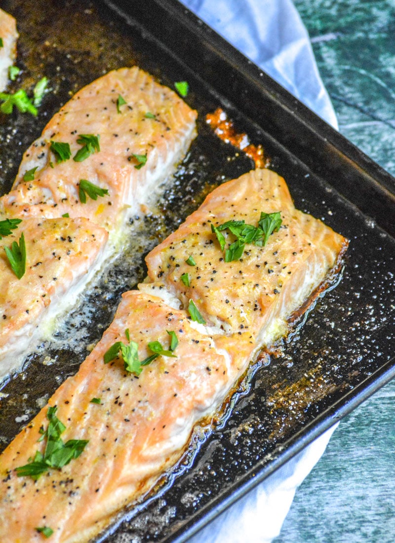 baked lemon pepper butter salmon filets on a metal baking sheet